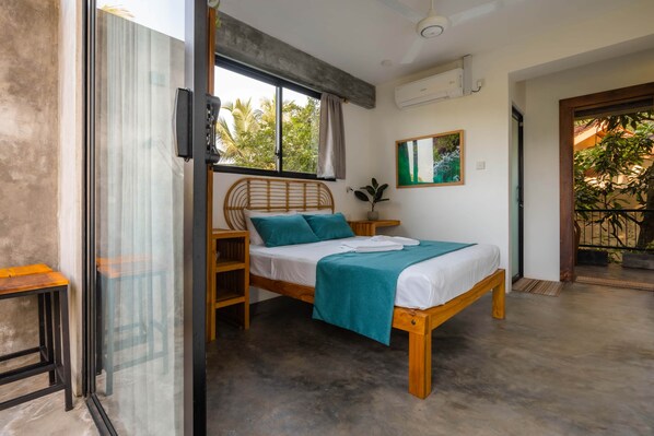 Une chambre à coucher comprenant un lit, une fenêtre, un climatiseur fixé au mur et une porte donnant sur un espace extérieur.