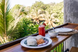 Un plateau avec une assiette de nourriture, un verre d’une boisson rouge et un bol sur un balcon donnant sur un paysage verdoyant.
