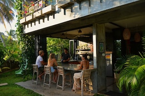 An outdoor bar area with a concrete structure, wicker chairs, and a person serving drinks.