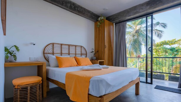 Quarto com cama, mesa de cabeceira e vista para palmeiras.