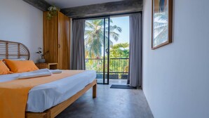 Quarto com cama, cabeceira de madeira, mesa de cabeceira, planta em vaso e vista para palmeiras através de uma porta de correr de vidro.