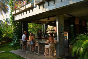 An outdoor bar area with a concrete structure, wicker chairs, and a person serving drinks.