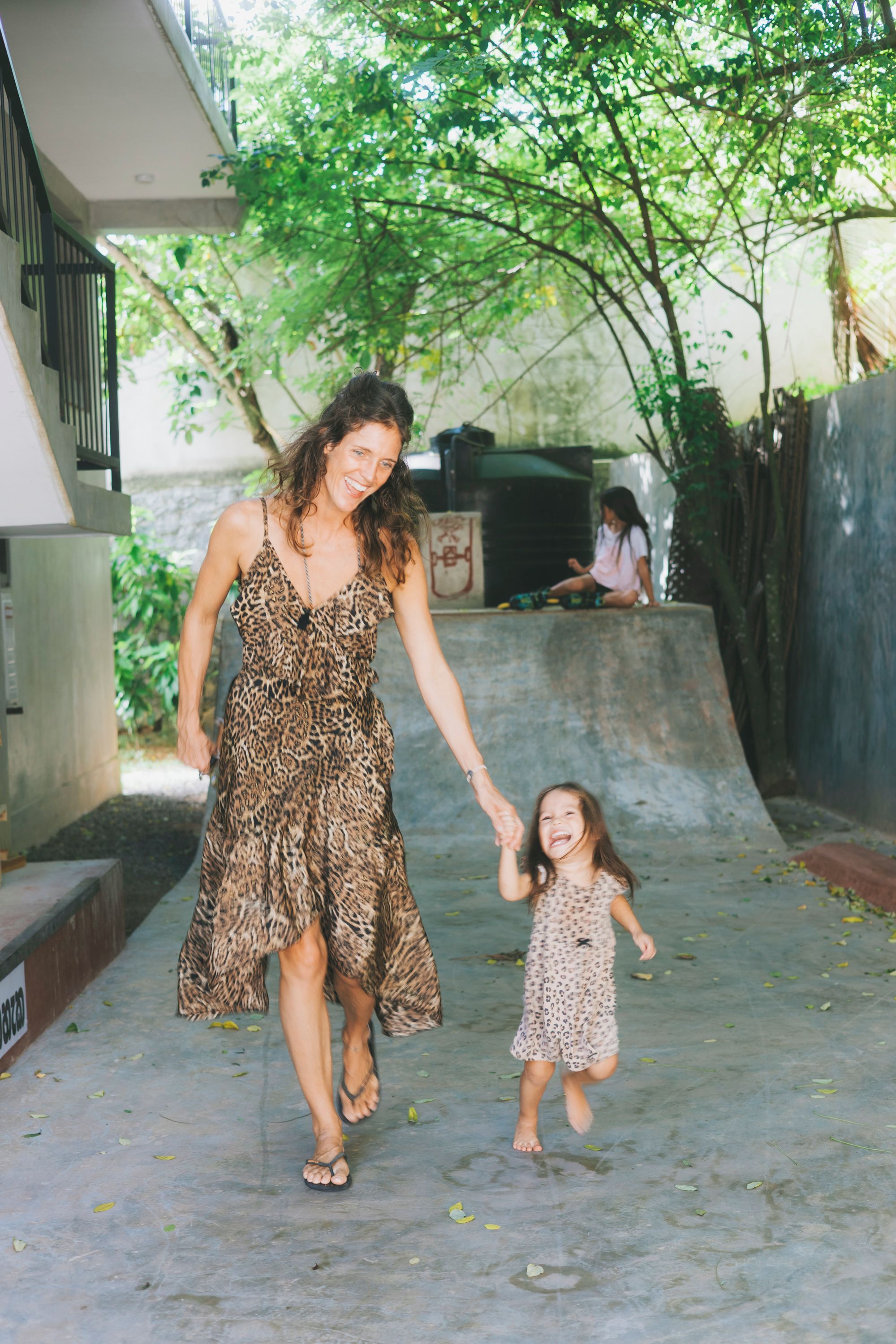 Mulher de vestido de leopardo caminhando com uma criança por um caminho de concreto.