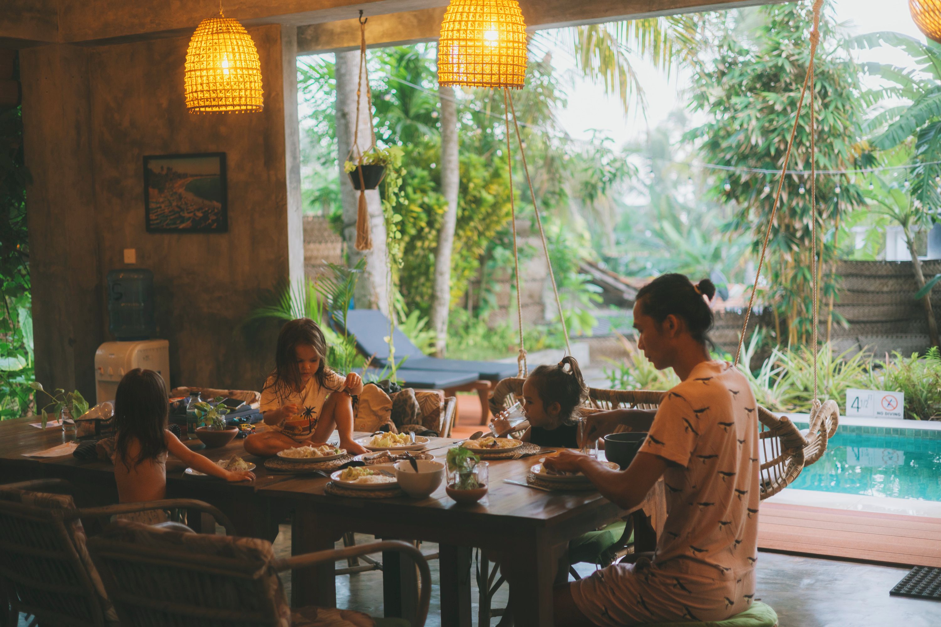 Un espace repas avec vue sur la piscine, doté de meubles en bois et d’éclairages suspendus.