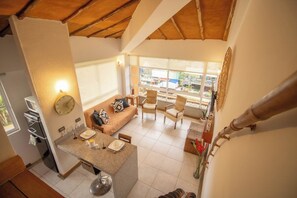 A spacious living area with a sofa, chairs, a dining table, and a kitchen area with a clock and a window.