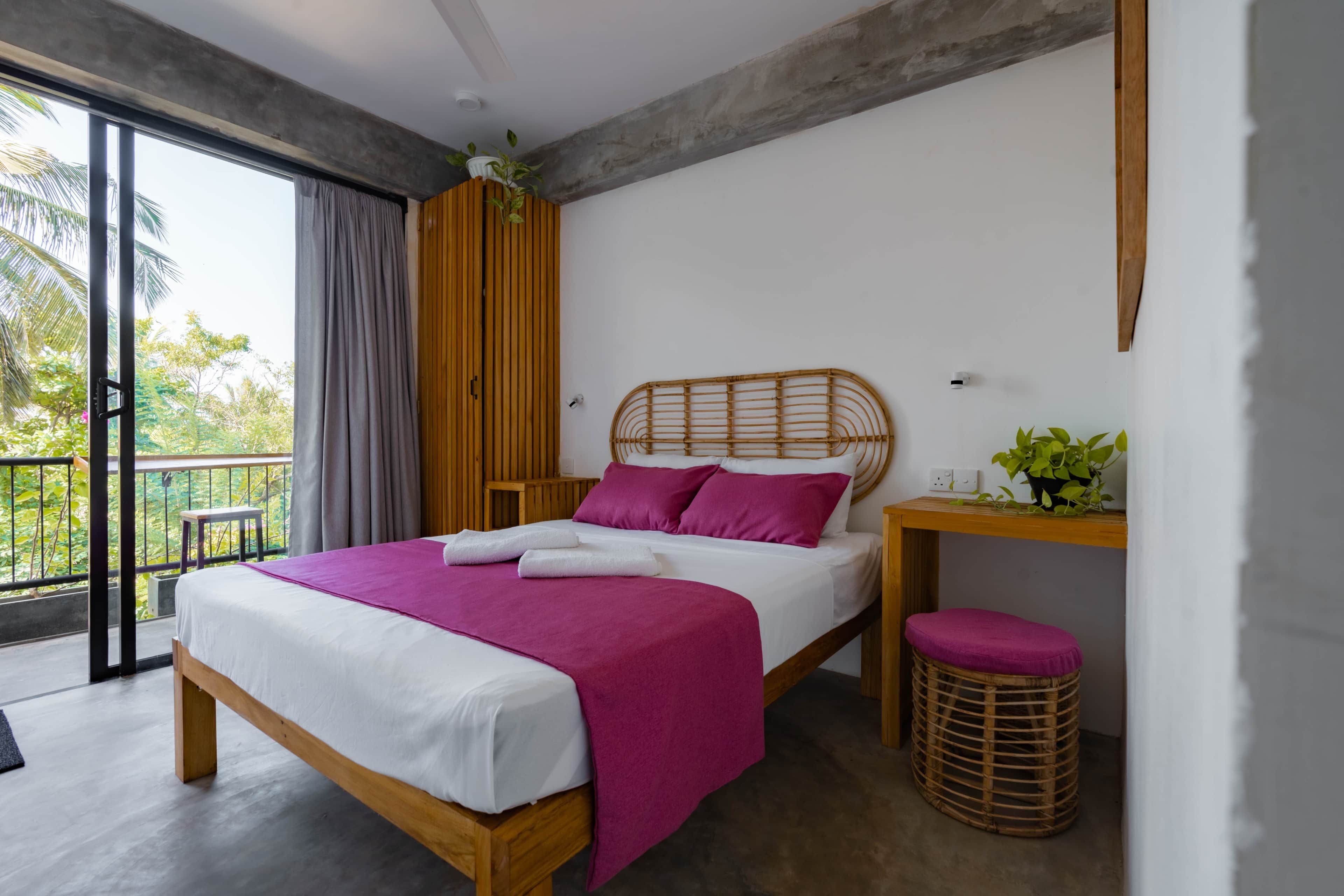 Ein modernes Schlafzimmer mit einem Holzbett, Balkonblick und einem kleinen Tisch mit einer Pflanze.