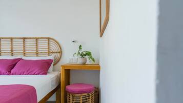 Una camera da letto con un letto, un comodino con una pianta, una lampada a parete e uno sgabello.