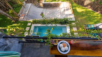 A rooftop pool with a stone border, surrounded by lush greenery and a bamboo fence.