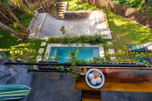 A rooftop pool with a stone border, surrounded by lush greenery and a bamboo fence.