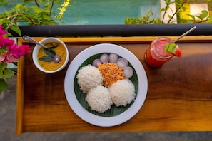 Prato de comida com arroz branco, uma tigela de sopa e uma bebida sobre uma mesa de madeira.