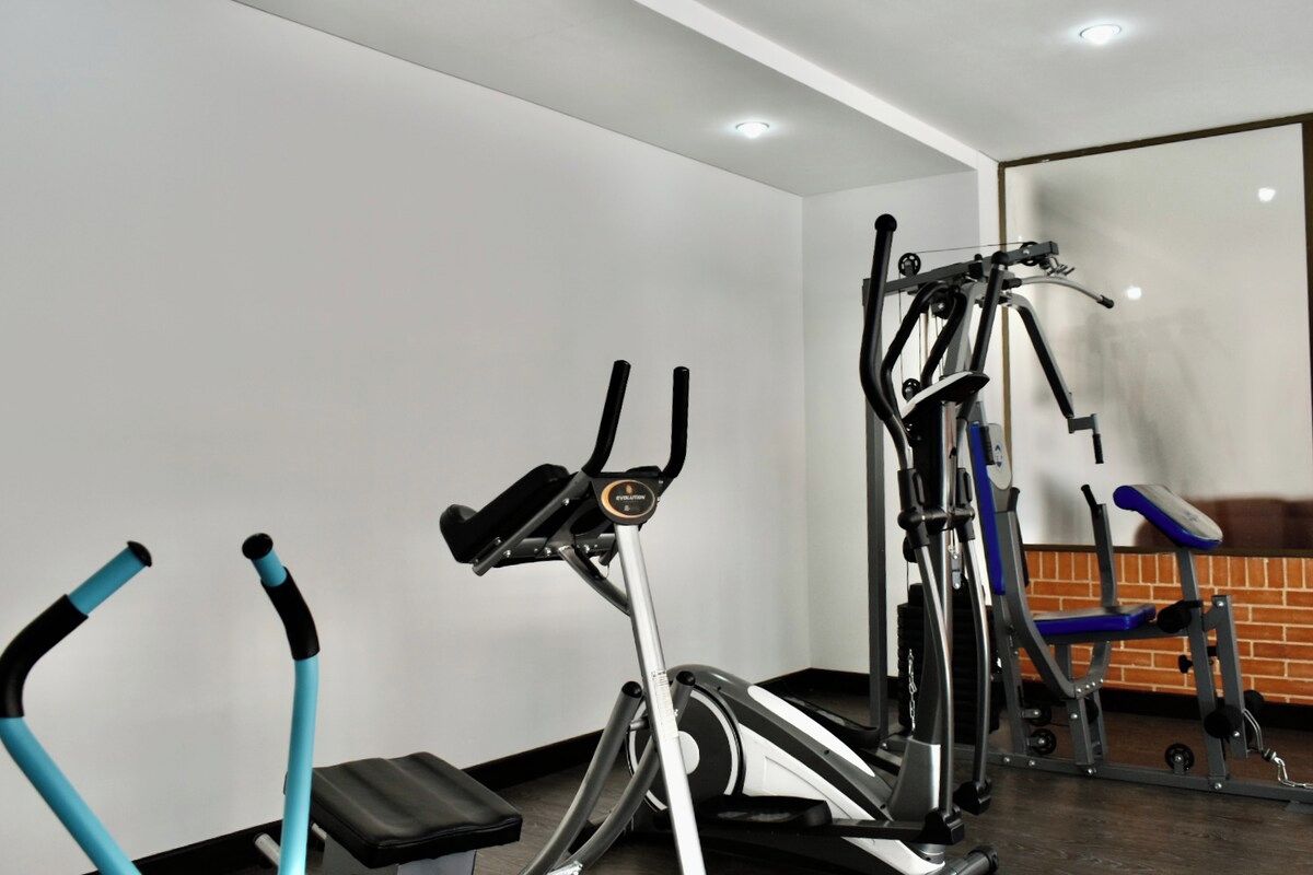Une salle de sport équipée de divers appareils, notamment un tapis de course, un vélo elliptique et des appareils de musculation.