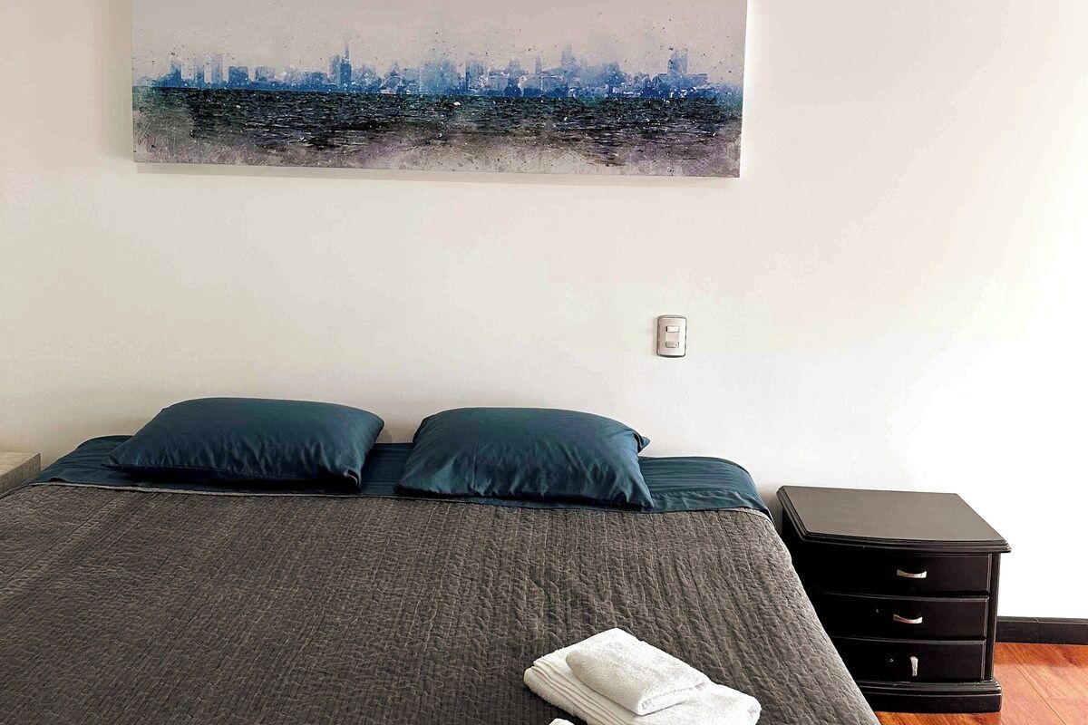 A bed with two pillows, a folded towel, and a nightstand with drawers.