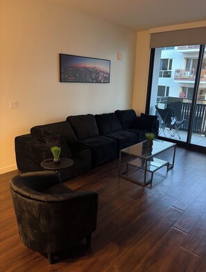 A living room with a black sofa, a round coffee table, and a chair. There is a cityscape painting on the wall and a view of a balcony with a chair. - Luxury Apartment In Downtown Tucson (Tucson)