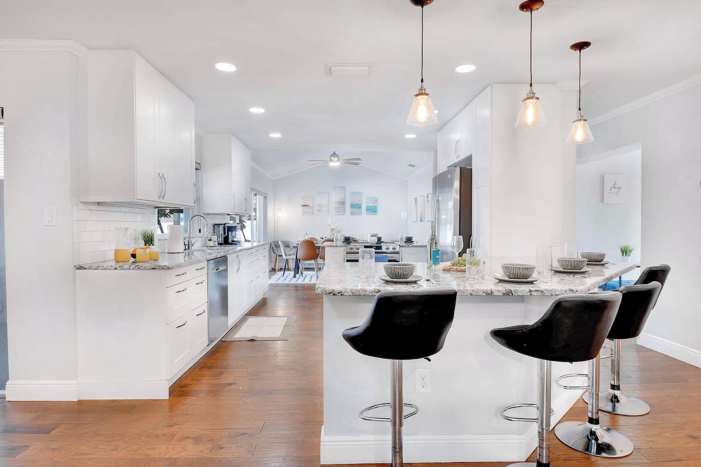 A modern kitchen with white cabinetry, a marble island, and black bar stools.