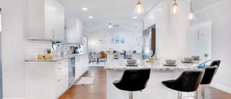 A modern kitchen with white cabinetry, a marble island, and black bar stools.