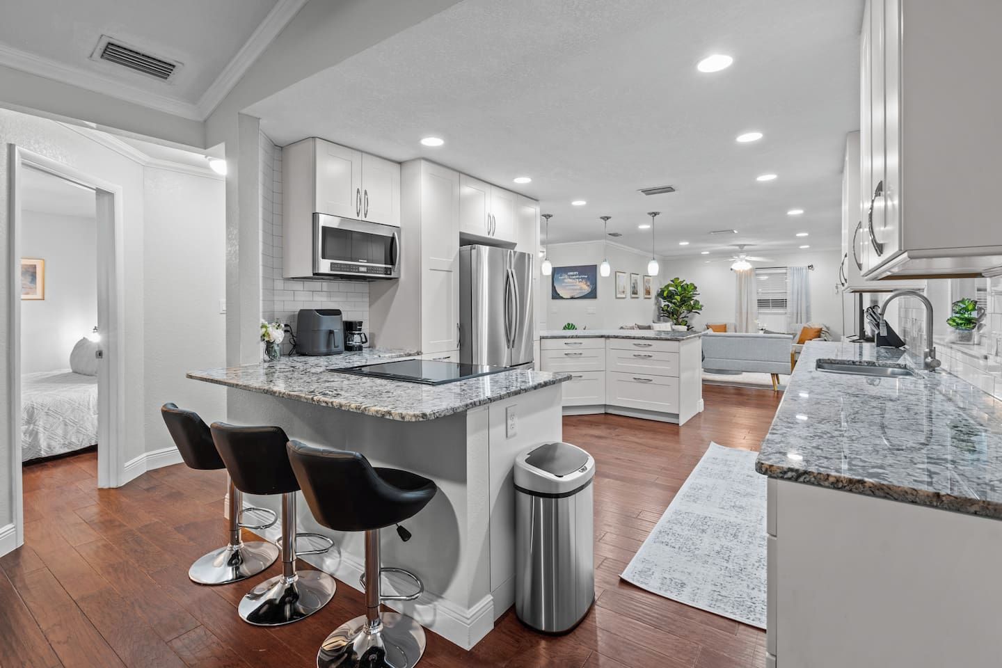 A modern kitchen with a central island, bar stools, a trash can, and a dining area with a sofa and table.