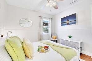 A bedroom with a bed, a bedside table, a mirror, a window with curtains, a ceiling fan, a painting, and a small plant. - Waterfront Escape: 5Bed, 3Bath, Heated Pool! (Tampa)