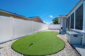 A backyard with artificial grass, a white fence, and a building with large windows. - Waterfront Escape: 5Bed, 3Bath, Heated Pool! (Tampa)