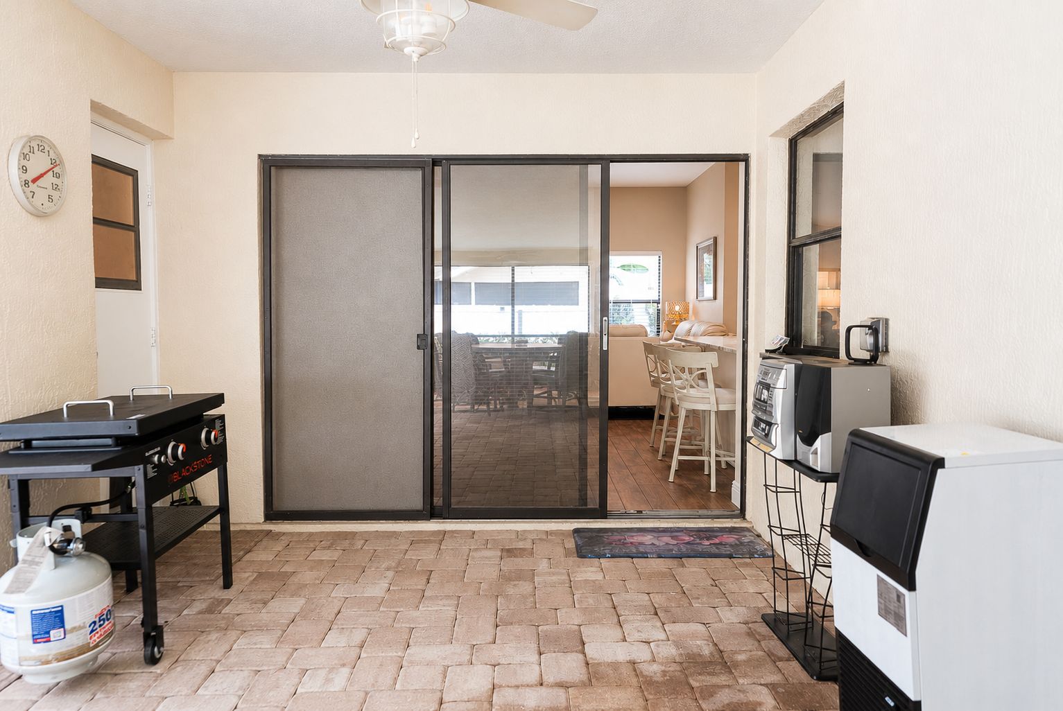 Un patio con puerta corrediza de vidrio que da a un área de estar exterior, una parrilla para barbacoa y un refrigerador.