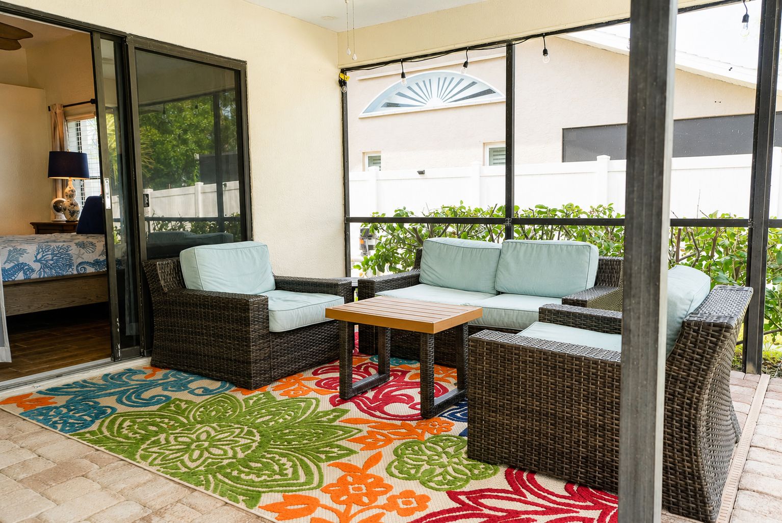 A covered patio with wicker furniture, a table, and a colorful rug.