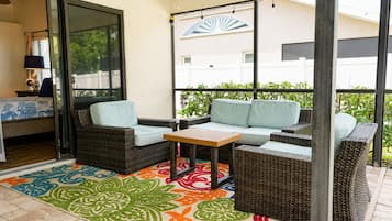 A covered patio with wicker furniture, a table, and a colorful rug.