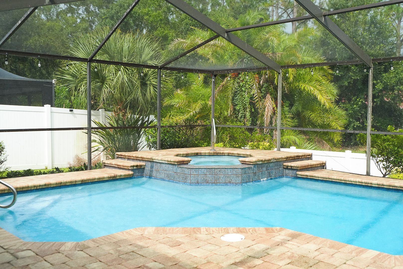 A swimming pool with a hot tub, surrounded by a covered area with a metal frame and glass panels.