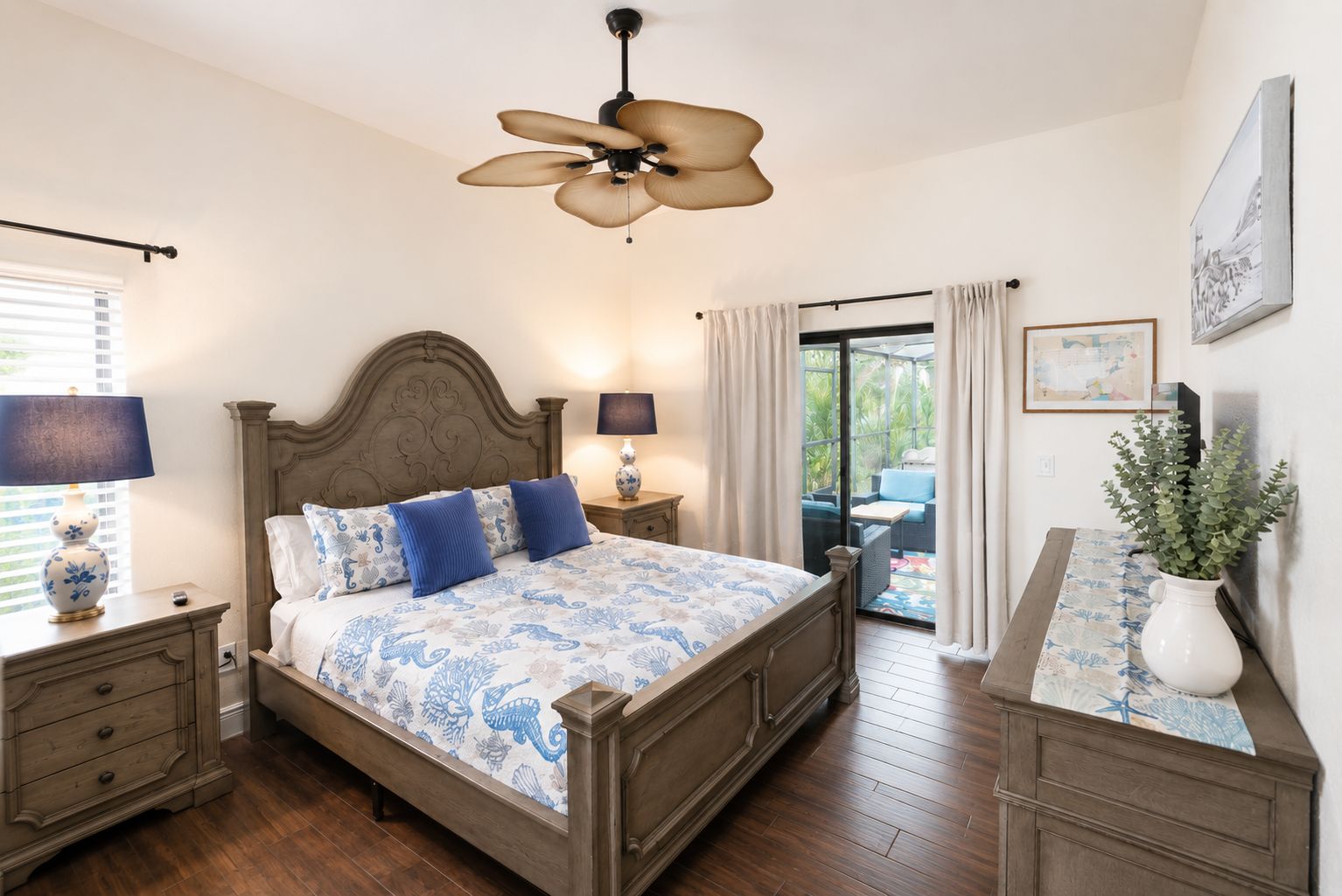 A bedroom with a bed, nightstands, a ceiling fan, a window with blinds, a view of the outdoors, and a potted plant.