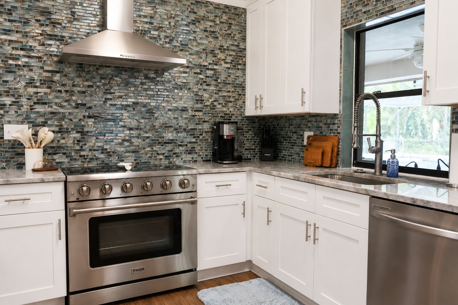 A modern kitchen with stainless steel appliances, white cabinetry, and a mosaic backsplash.