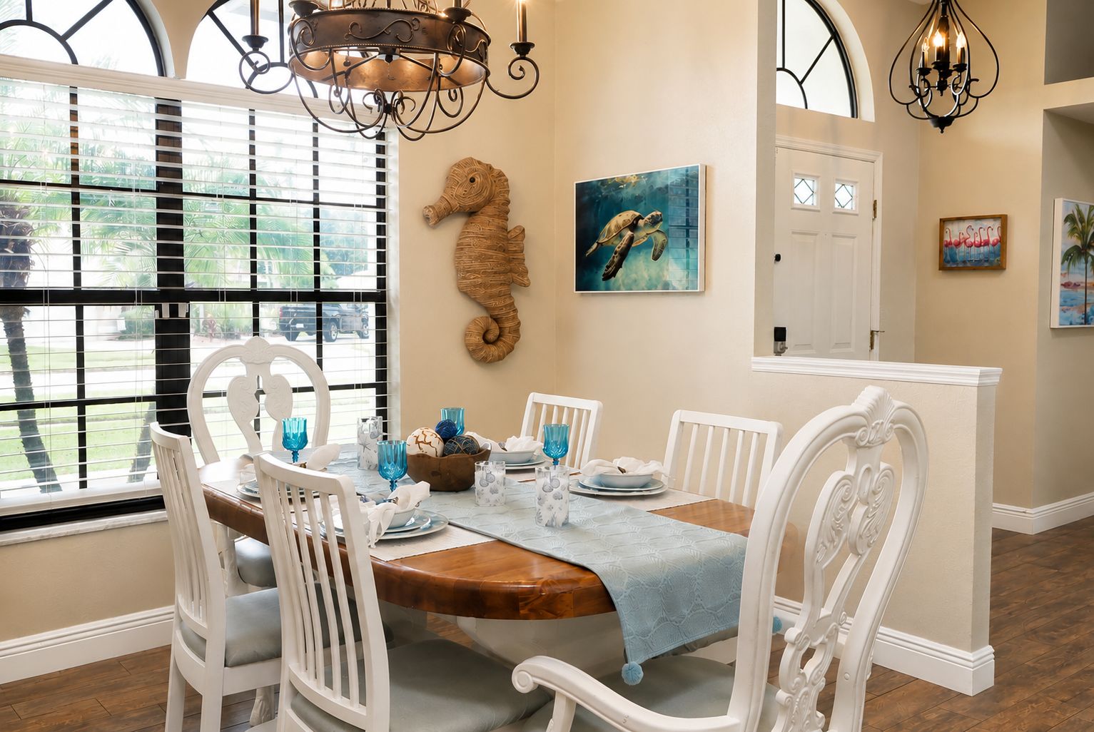 A dining area with a wooden table, white chairs, and a seahorse wall decoration.