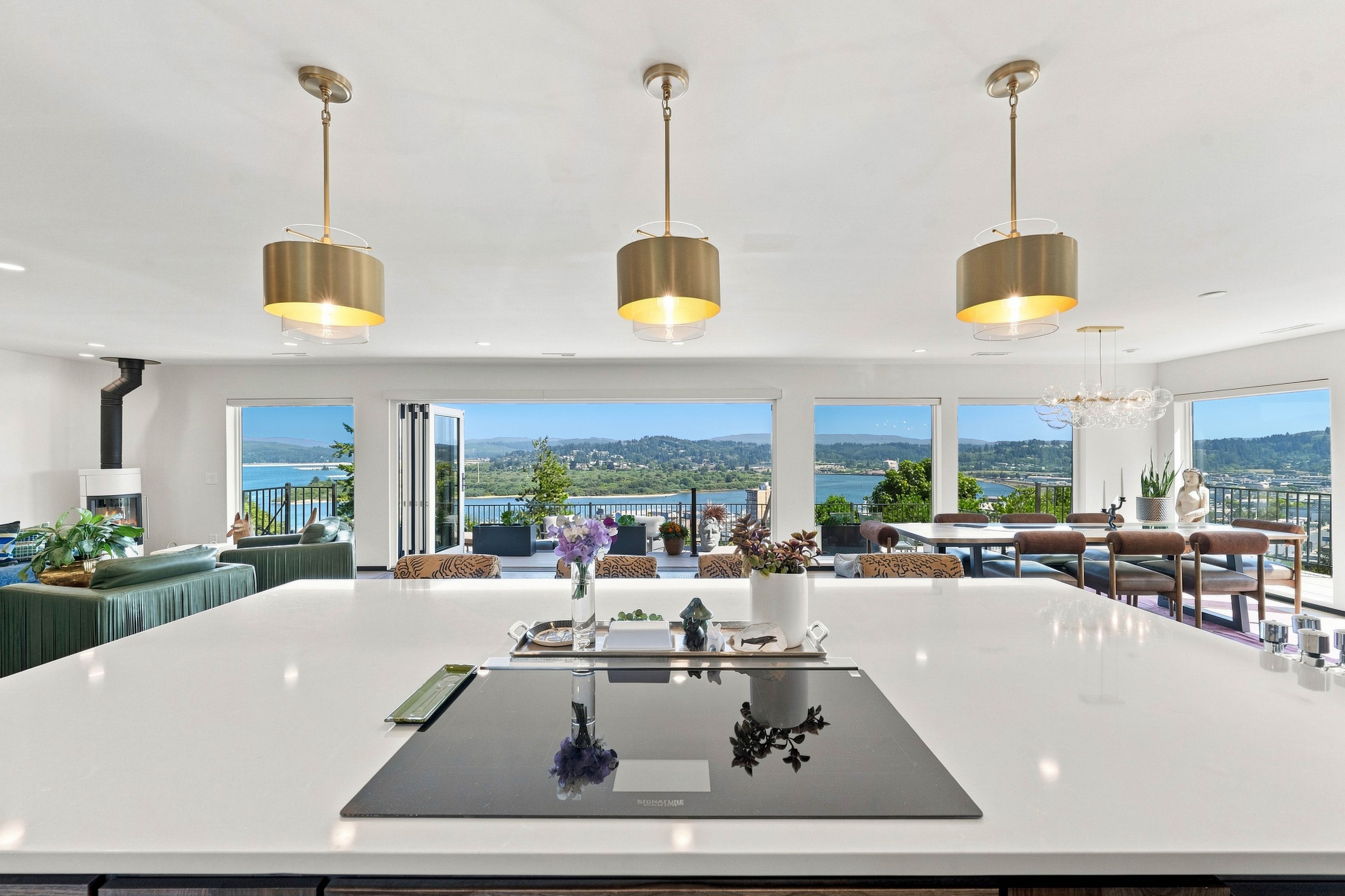 A spacious kitchen with a central island, large windows offering a scenic view, and three pendant lights.