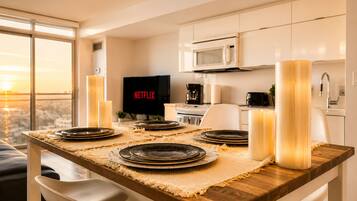 A modern dining area with a wooden table set for four, a TV displaying Netflix, and a city view through large windows.