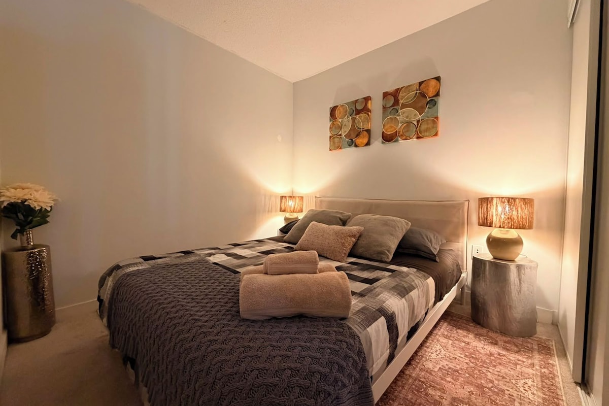 Une chambre à coucher comprenant un lit, deux œuvres d’art murales, deux lampes de chevet, un vase avec des fleurs et un tapis.