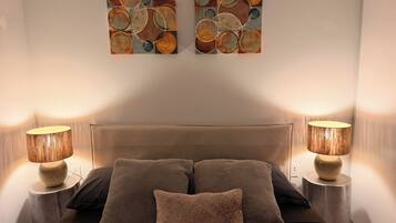 A bedroom with a bed, two wall-mounted lamps, and two abstract paintings.