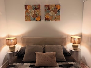 Un dormitorio con una cama, dos lámparas de pared y dos cuadros abstractos.