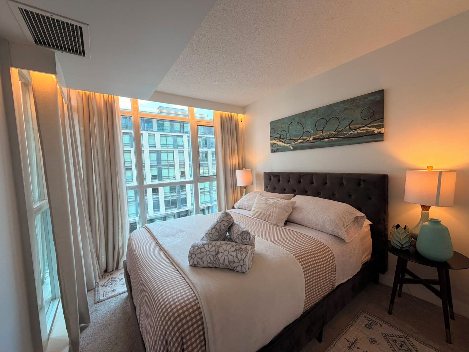 Une chambre d’hôtel avec un grand lit, une fenêtre avec des rideaux, une œuvre d’art accrochée au mur et une lampe de chevet.