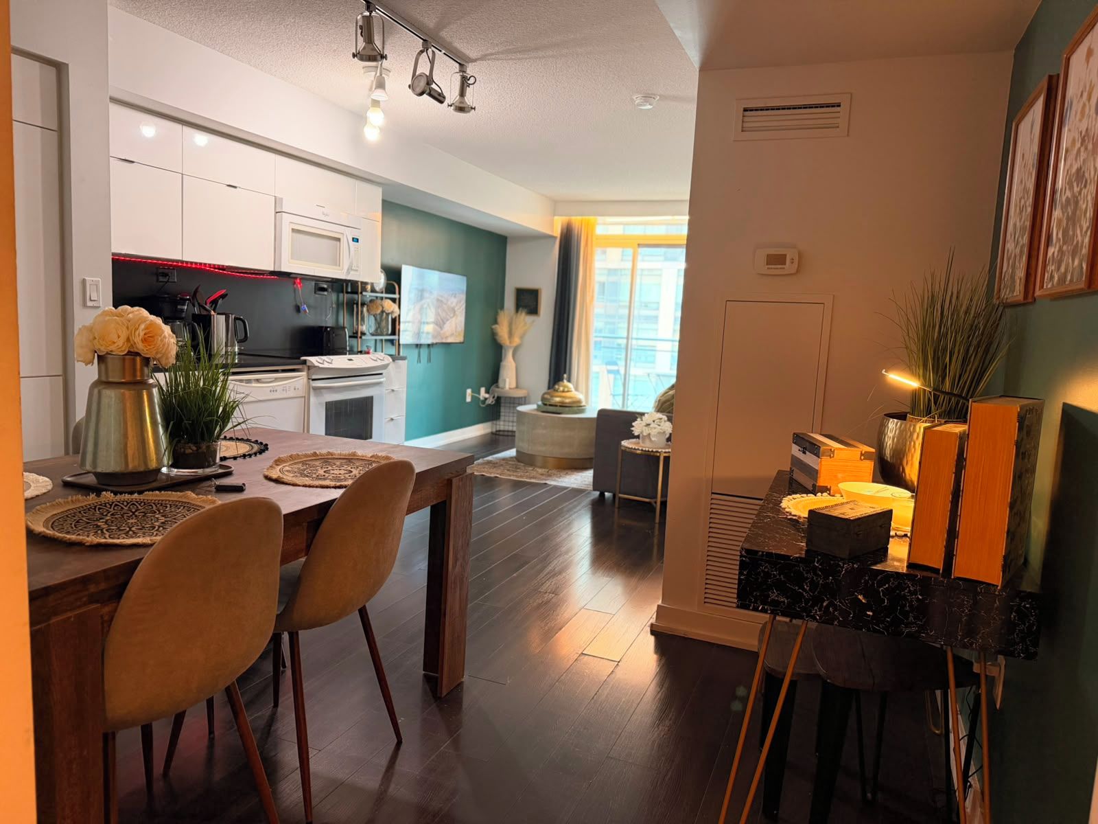 A modern kitchen with white cabinets, a dining area with a wooden table and chairs, and a living space with a sofa and a coffee table.
