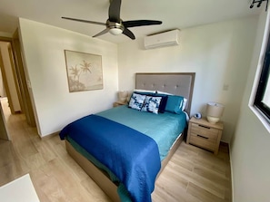 A bedroom with a bed, a ceiling fan, an air conditioning unit, a nightstand, and a wall-mounted lamp. - The Beach - Crystal Lagoon Waterfront - Sleeps 10 (Punta Cana)