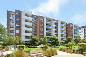 A multi-story residential building with balconies, a courtyard with benches, and a well-maintained garden. - Modern 1BR and Study Near Airport Shops & Parking (Botany)