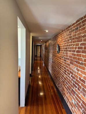 A hallway with wooden flooring, a brick wall, and a door at the end. - Historic Home Away From Home (Indianapolis)
