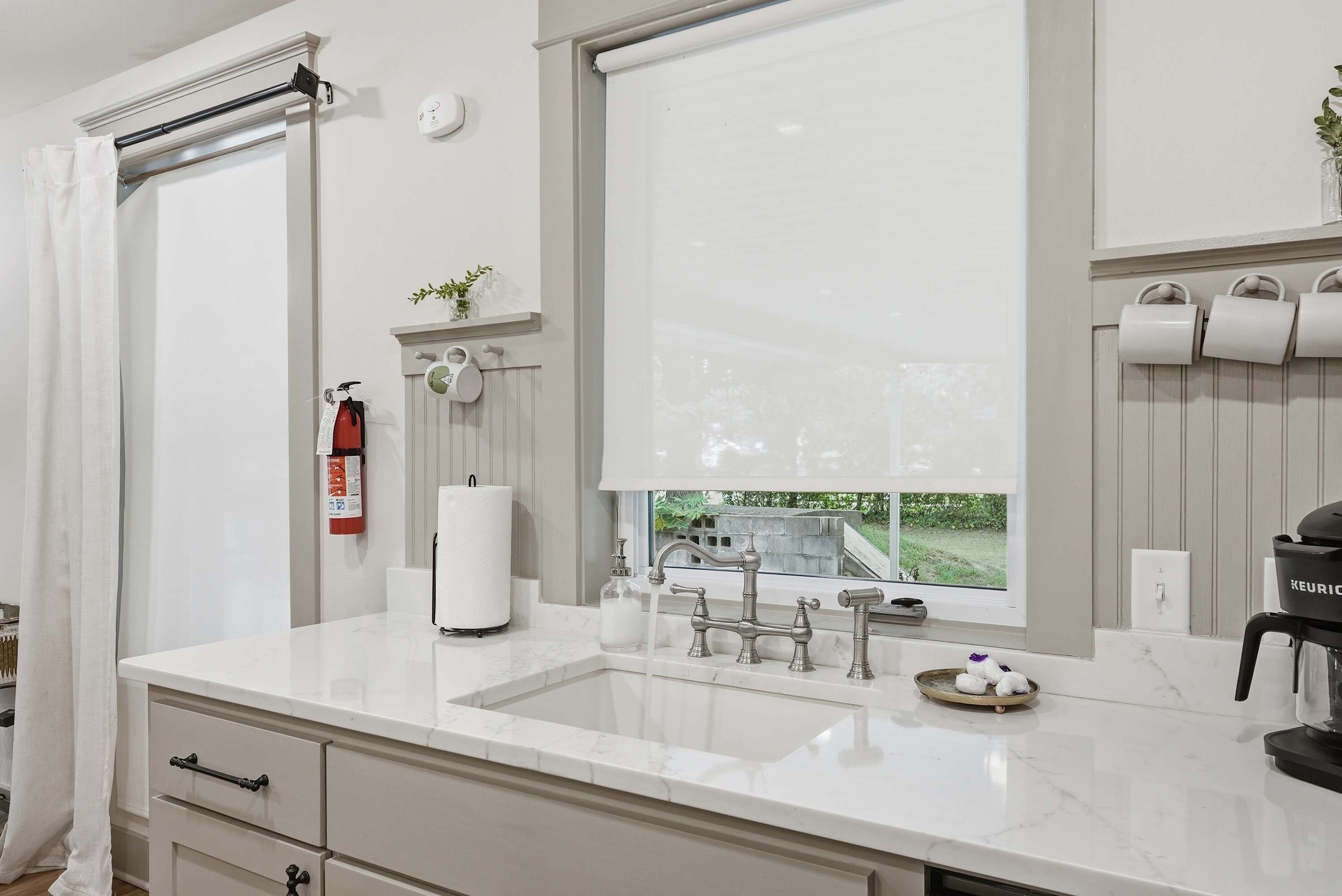 Een moderne badkamer met een groot raam, een wastafel met een marmeren blad, een toiletrolhouder en een brandblusser.