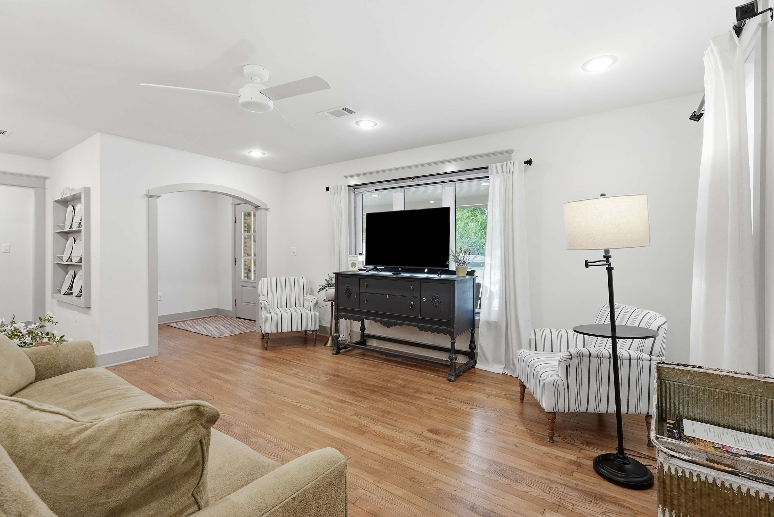 Una sala de estar con sofá, televisor, mueble, lámpara y ventilador de techo.