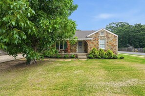 A stone house with a front porch, a small lawn, and a tree to the left. - Respite Cottage - Front Porch - Sunroom - 1 mi UCA (Conway)