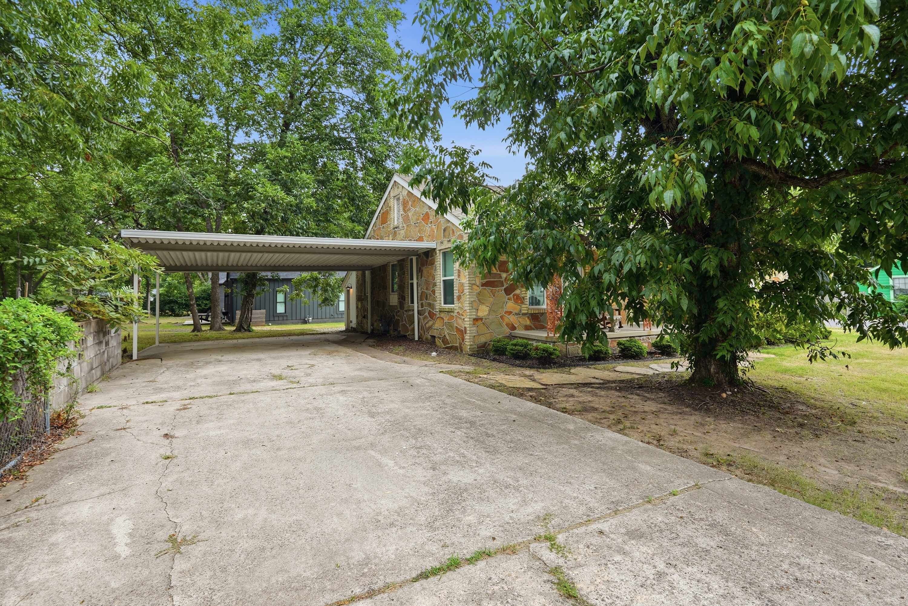 Un bâtiment en pierre avec une allée couverte et un grand arbre devant.