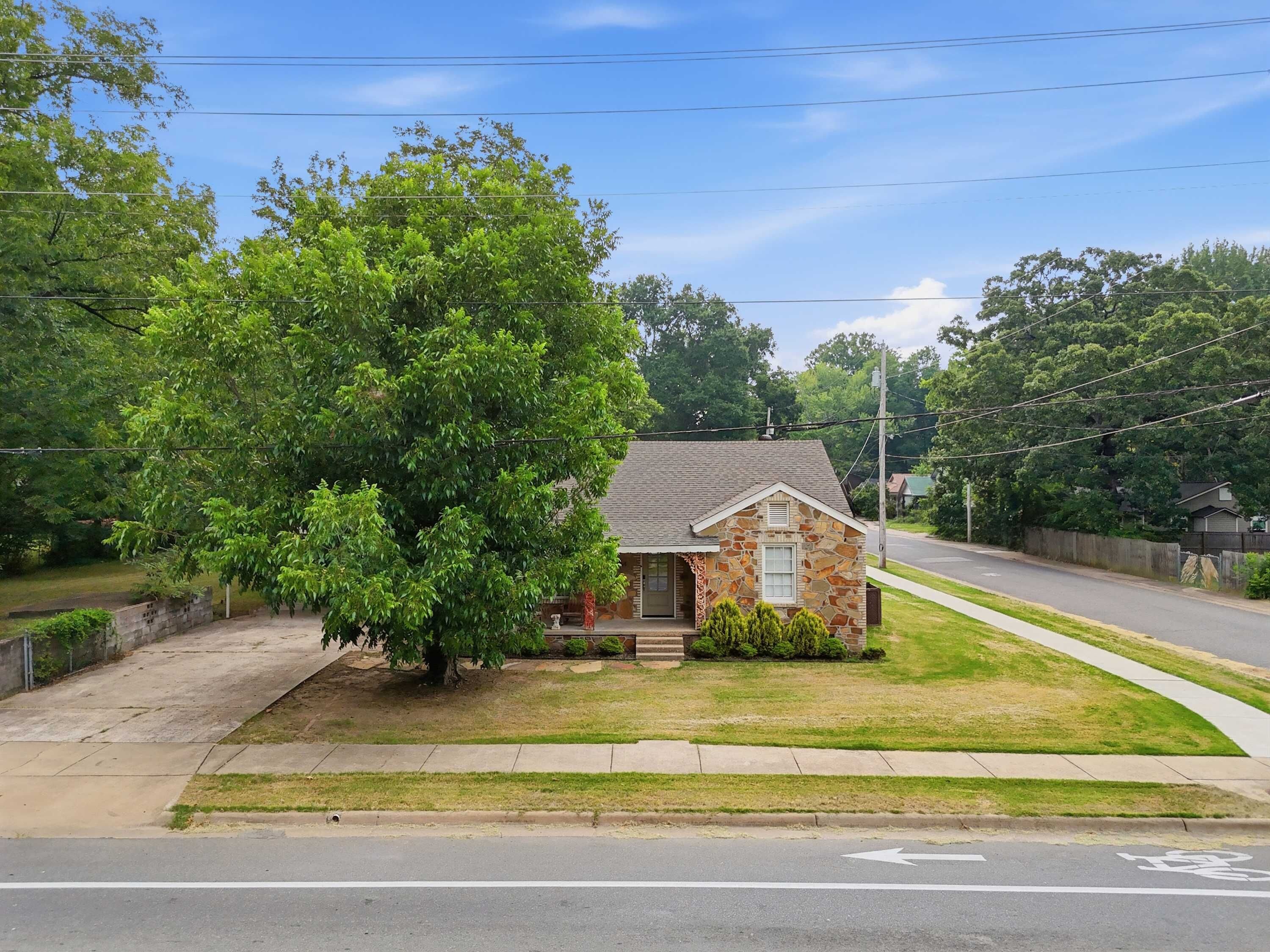 A small stone house with a grassy yard and a sidewalk leading to a road.