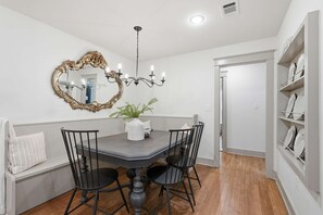 A dining area with a round table, black chairs, a chandelier, a mirror with an ornate frame, and a white vase with green foliage. - Respite Cottage - Front Porch - Sunroom - 1 mi UCA (Conway)