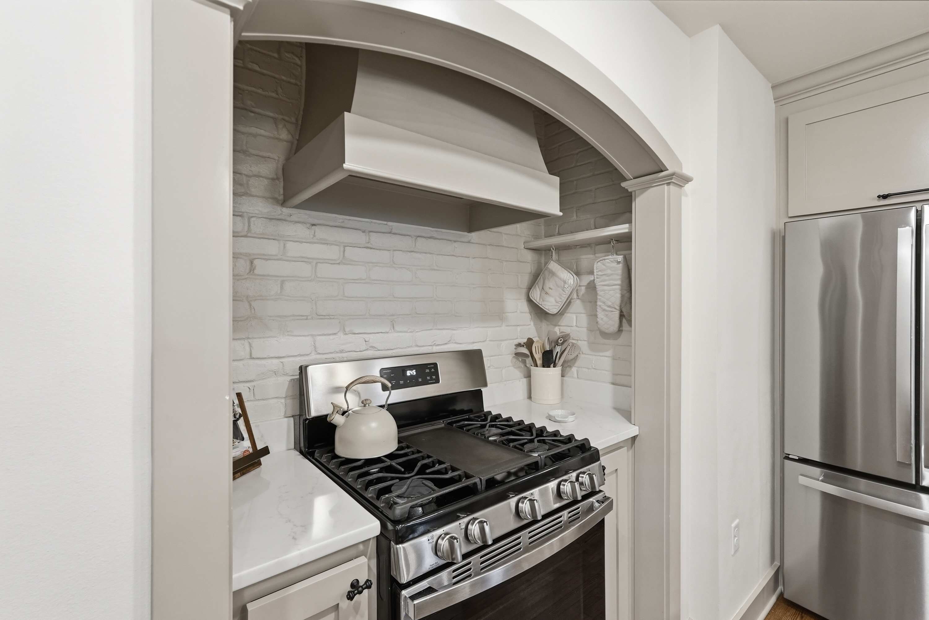 A kitchen with a stainless steel stove, a white brick backsplash, and a stainless steel refrigerator.