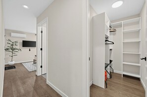 A hallway with a potted plant, a flat-screen TV, and a white door leading to a room with a built-in wardrobe and shelves. - Stylish 3BR Seattle Retreat near UW w/ City Views (Seattle)