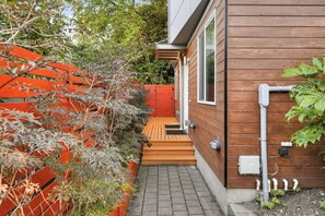Une maison moderne avec une façade en bois, une clôture rouge et un chemin pavé menant à l’entrée.