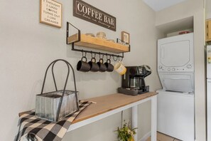 A kitchen area with a coffee bar, a coffee maker, and a hanging mug rack. - Cozy Lake View Condo: Farmhouse Vibes & Views • Walk to Marina! (Branson)