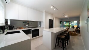 Eine moderne Küche mit weißen Schränken, einer zentralen Kochinsel mit Barhocker und einem Essbereich mit Tisch und Stühlen.